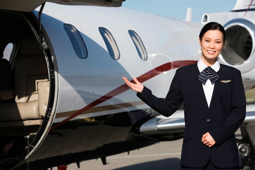 A female steward waiting for passengers next to a private jet door