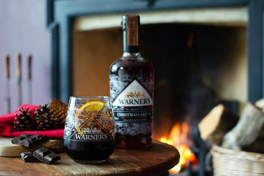 A bottle of the Christmas Cake Gin with freshly poured glass by a roaring fireplace