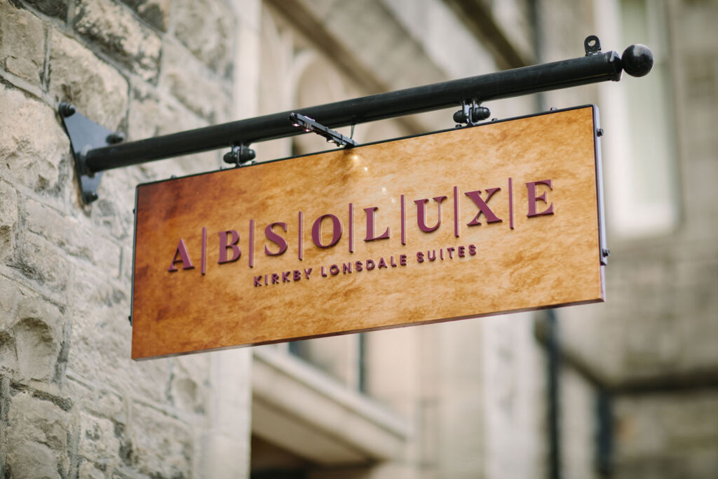 The wooden sign hanging outside the building with Absoluxe engrained on it