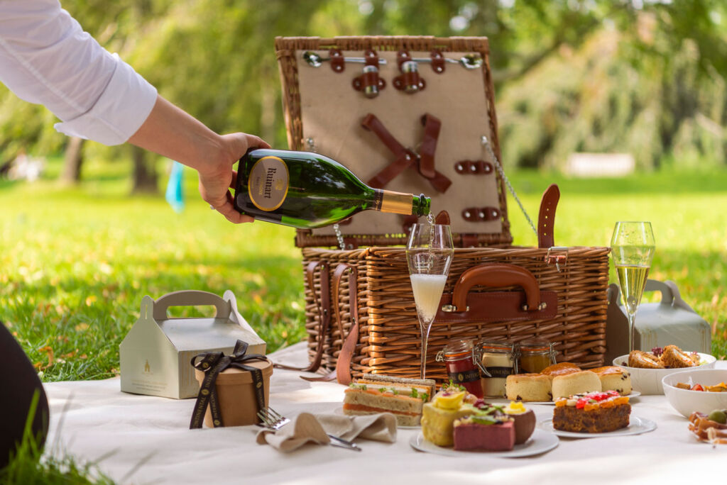 Someone pouring a glass of bubbly with their exceptional picnic hamper