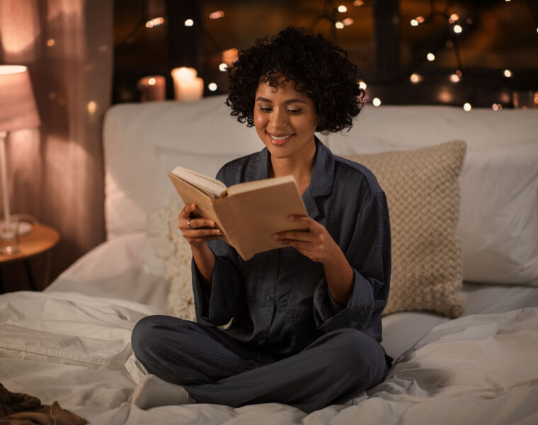 A woman reading a book on her bed at night before going to bed