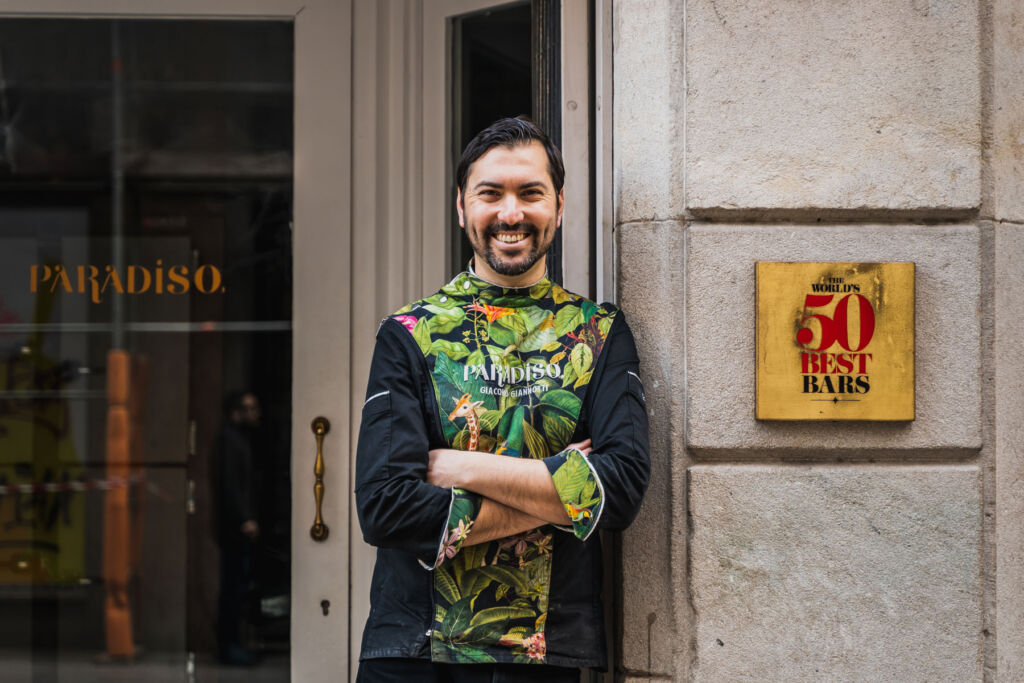 Giacomo standing outside his bar with a gold plaque acknowledging the bar's achievements