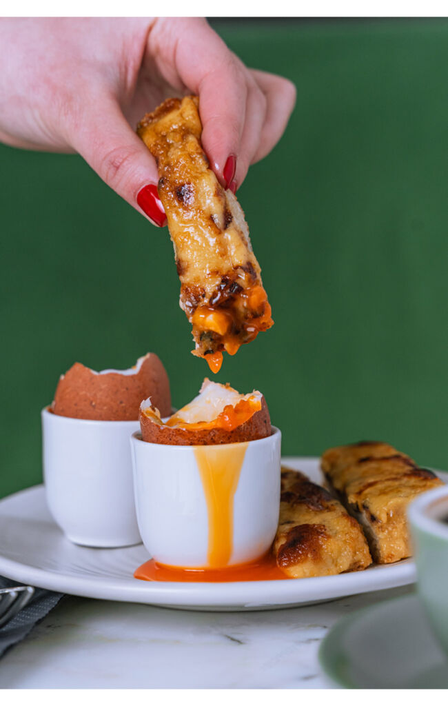 A photograph showing a patron dipping a savoury into a soft boiled egg