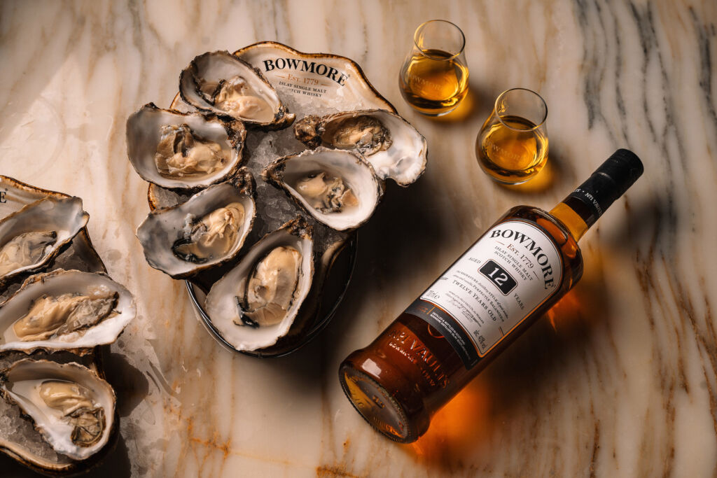 A bottle of the whisky placed on a marble table next to a plate of oysters