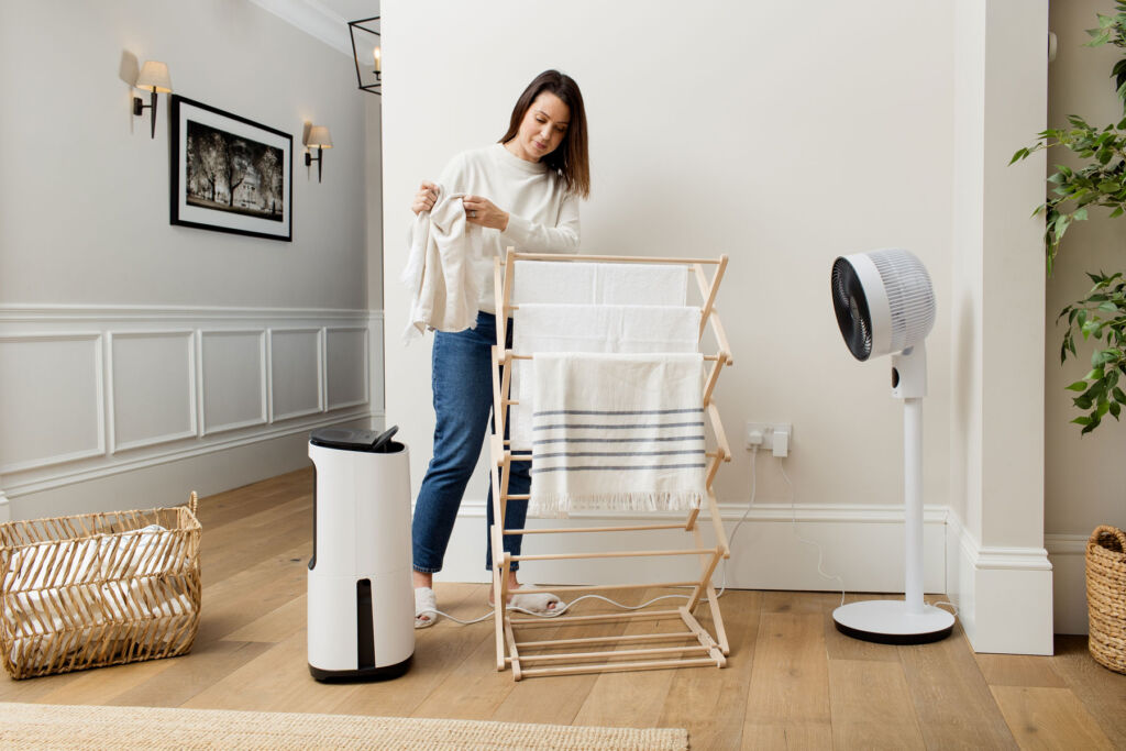 A woman drying clothes using the fan and one of the company's dehumidifiers