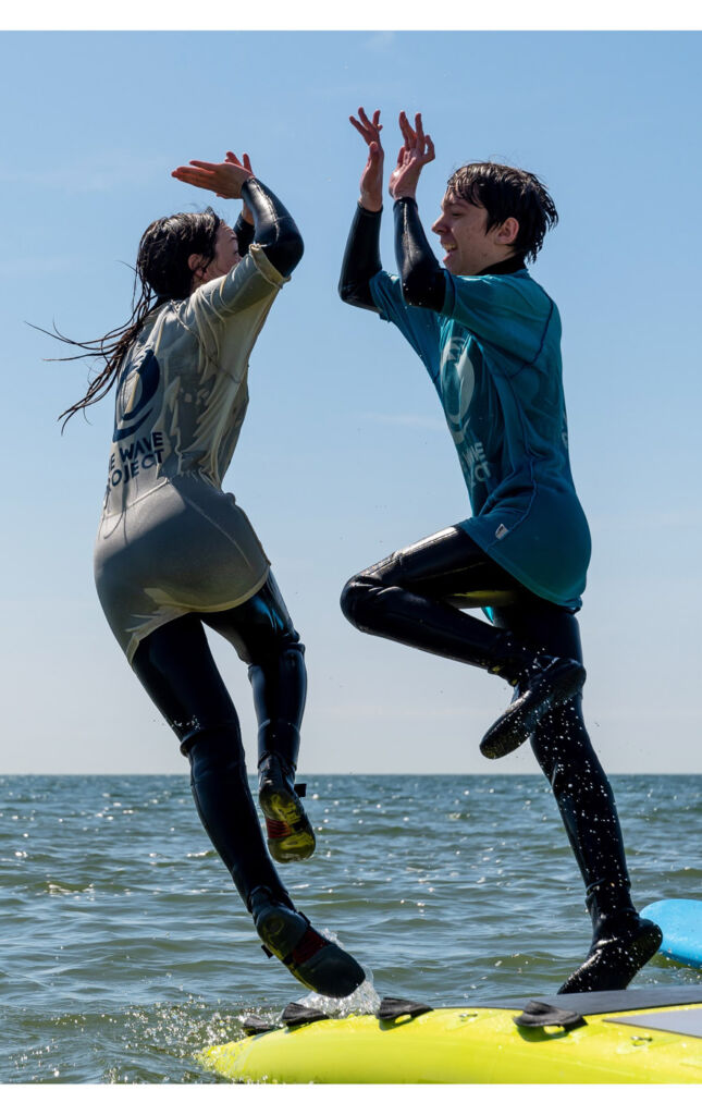 Young people high-fiving while jumping off a surfboard