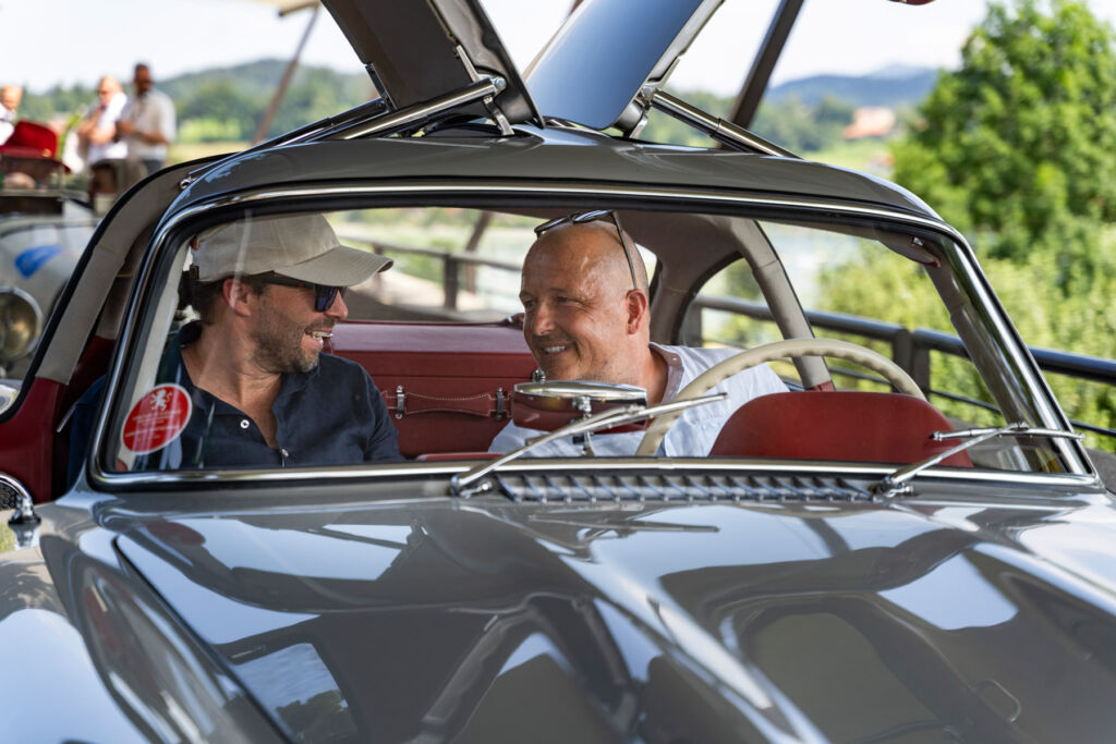 Two men engaged in conversation in a gullwing Mercedes