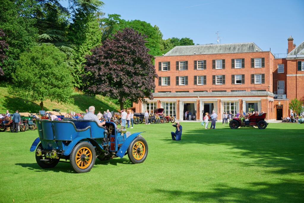 A vintage car being photographed outside the historic house