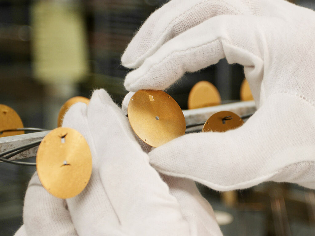 A member of the watchmaking team inspecting the gold dials wearing white gloves