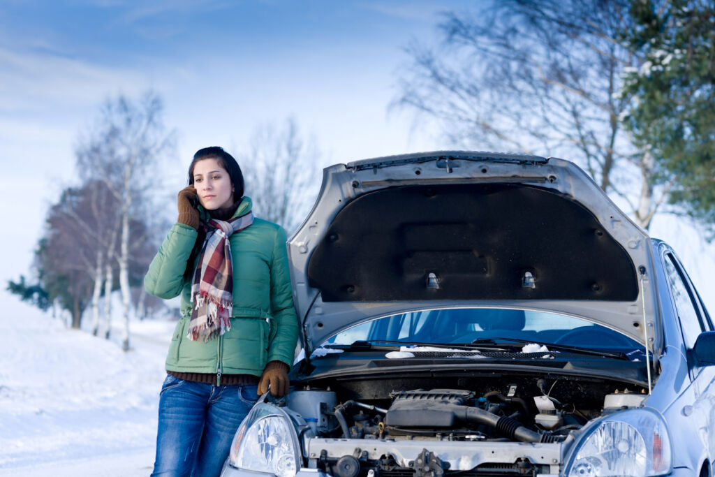 A woman next to a car that has broken down in the snow