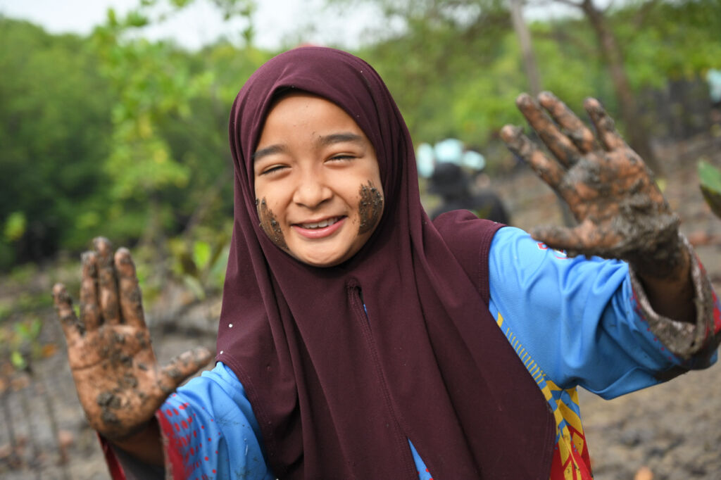 A happy young girl with mud on her hands face after the planting