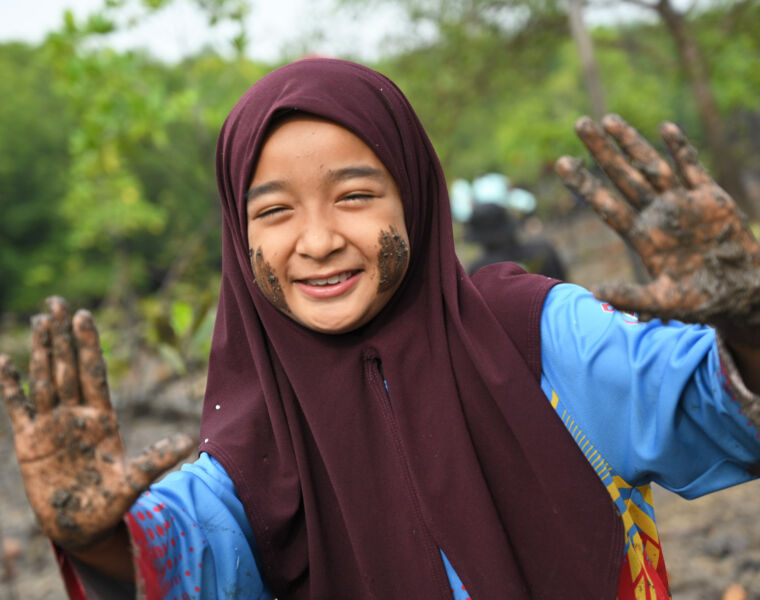 A happy young girl with mud on her hands face after the planting