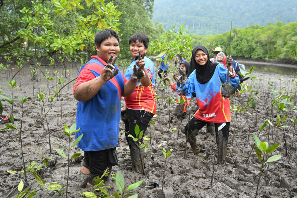 Volunteers standing in knee deep mud, planting the trees