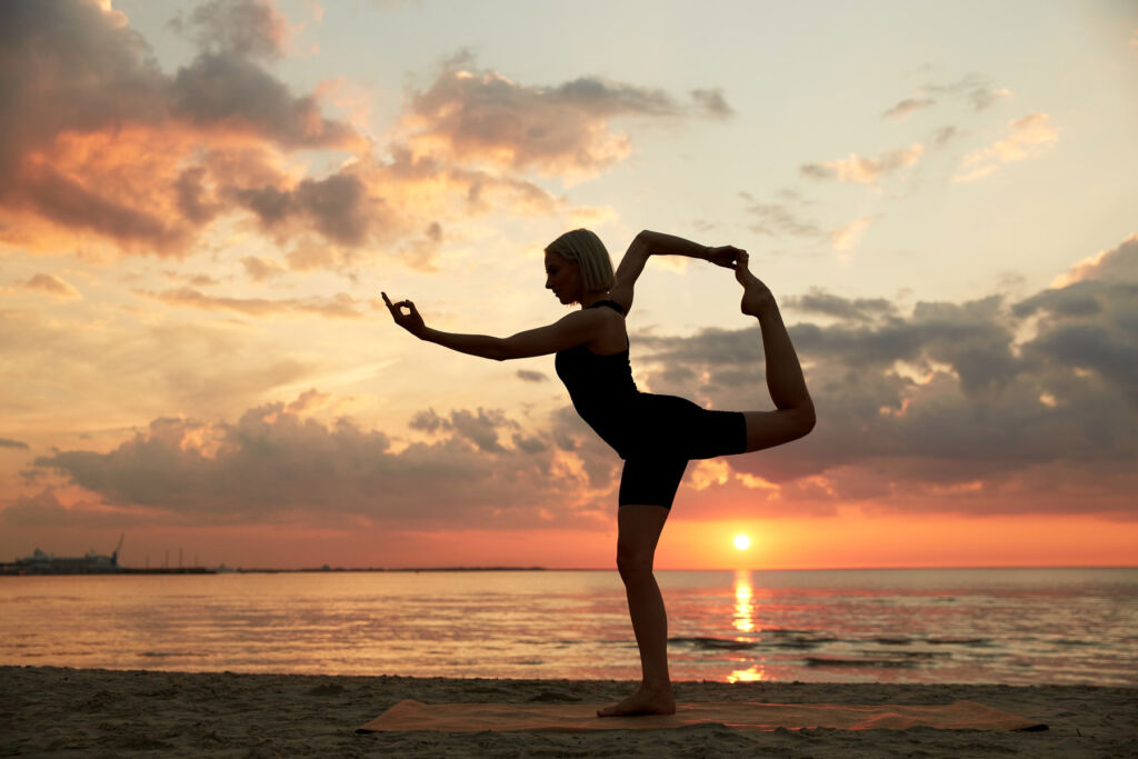 A woman doing a yoga pose on a beach at sunset