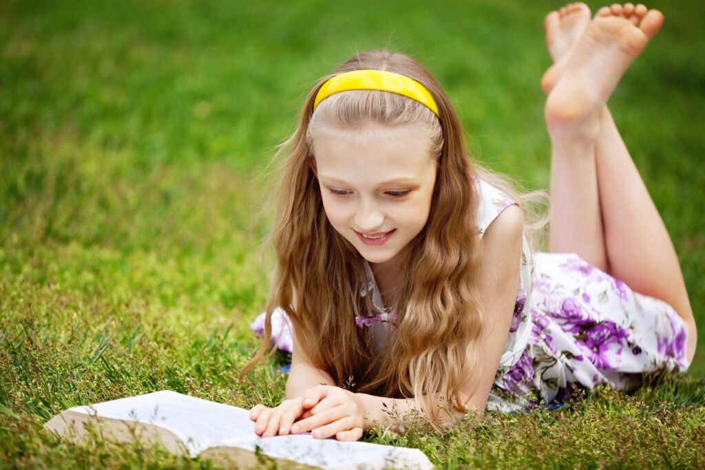 A young girl laying on the grass reading a book