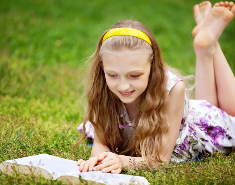 A young girl laying on the grass reading a book