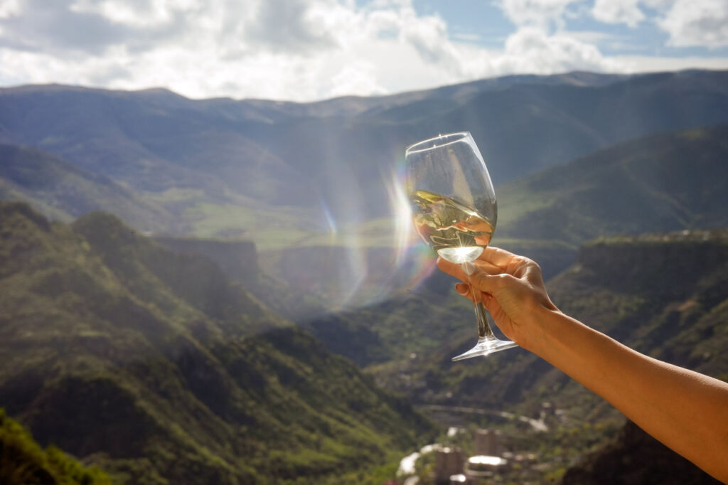 A glass of wine being held with the sun shining in the background