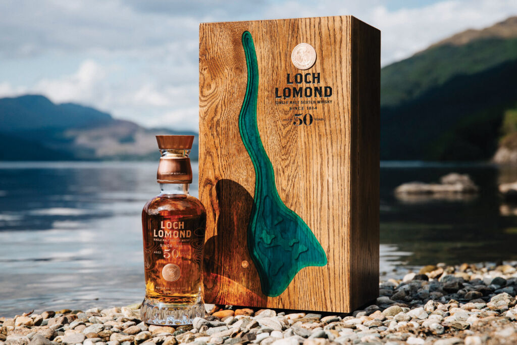 The bottle next to its beautiful wooden case on the shore of the Loch