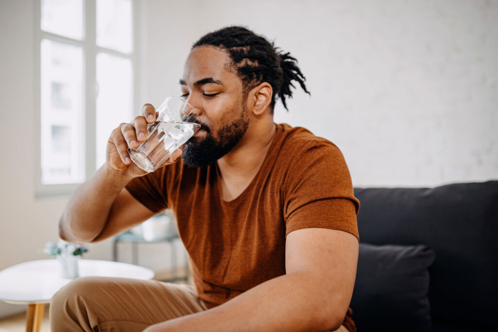 A man sat on a chair drinking a glass of water