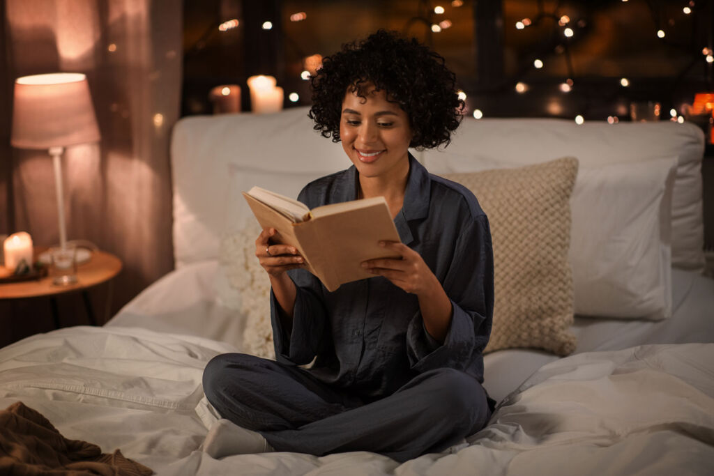 A woman reading a book while sat on her bed