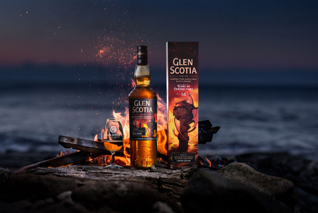 A bottle of the whisky in front of a fire on the shore at night