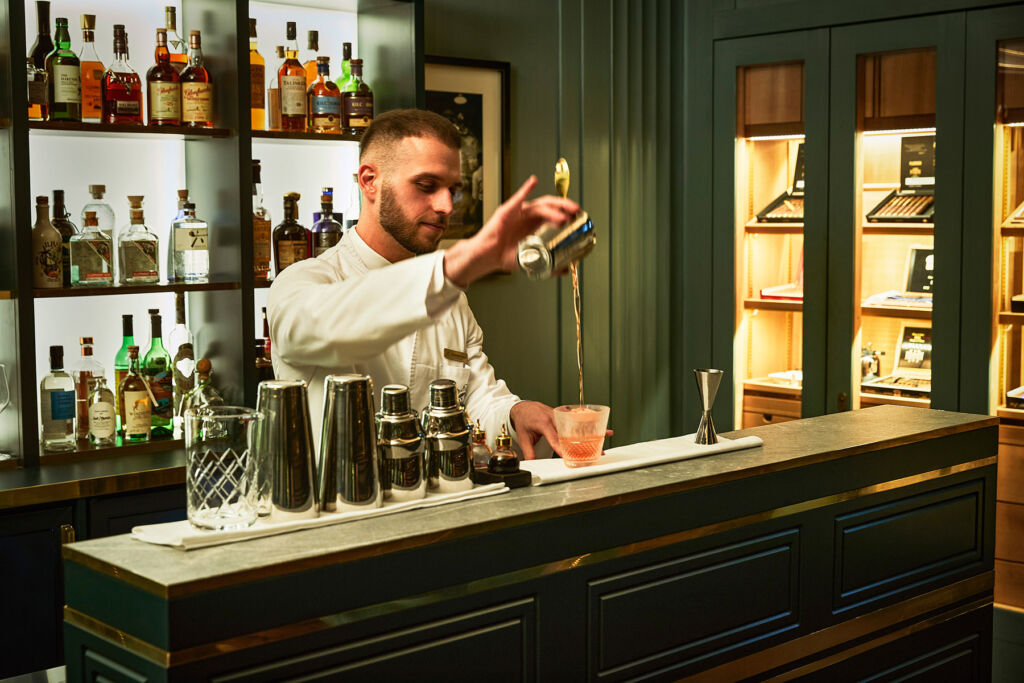 A bartender high-pouring a cocktail