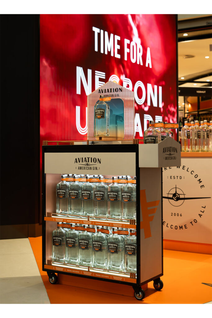 A cabinet filled with gin in front of a sign encouraging travellers to try a Negroni