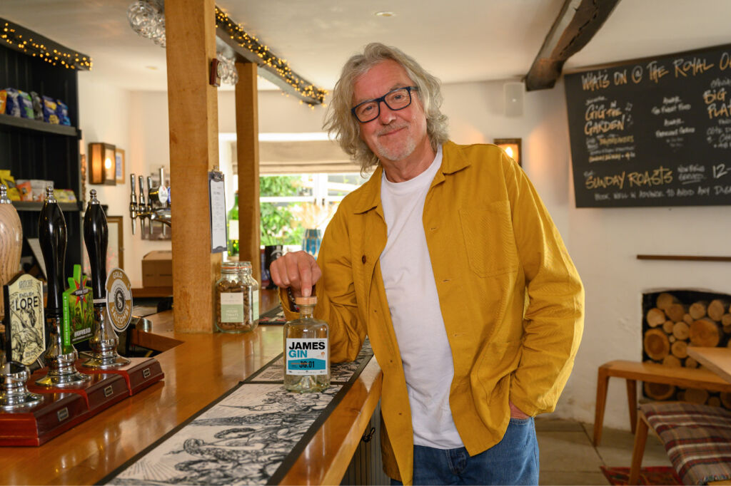 James proudly holding a bottle of his gin in a public house bar