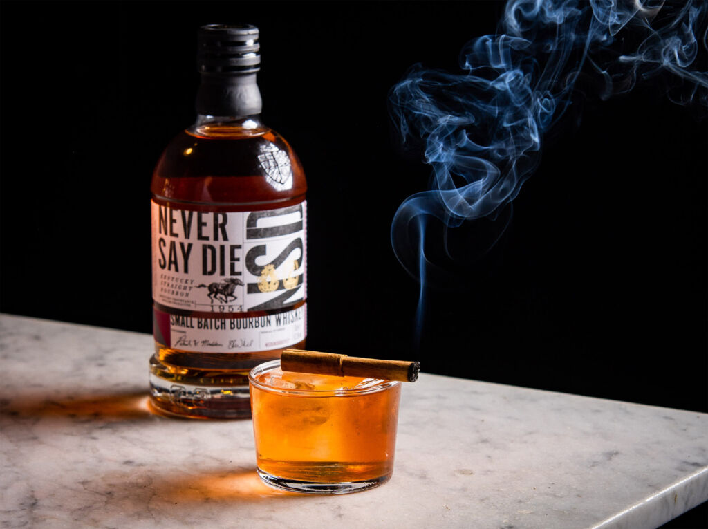 A bottle of the Never Say Die bourbon next to a full glass