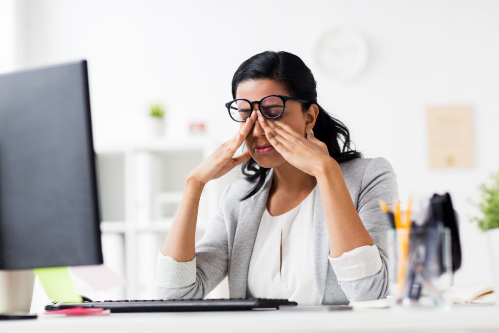 A woman rubbing her eyes from behind her computer screen