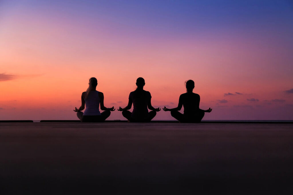 Three female guests meditating on the beach at sunset