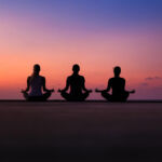 Three female guests meditating on the beach at sunset