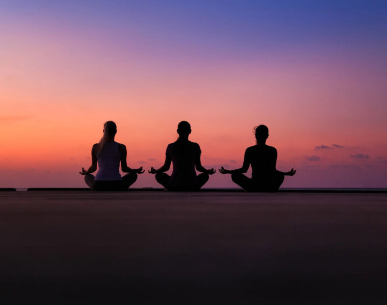 Three female guests meditating on the beach at sunset